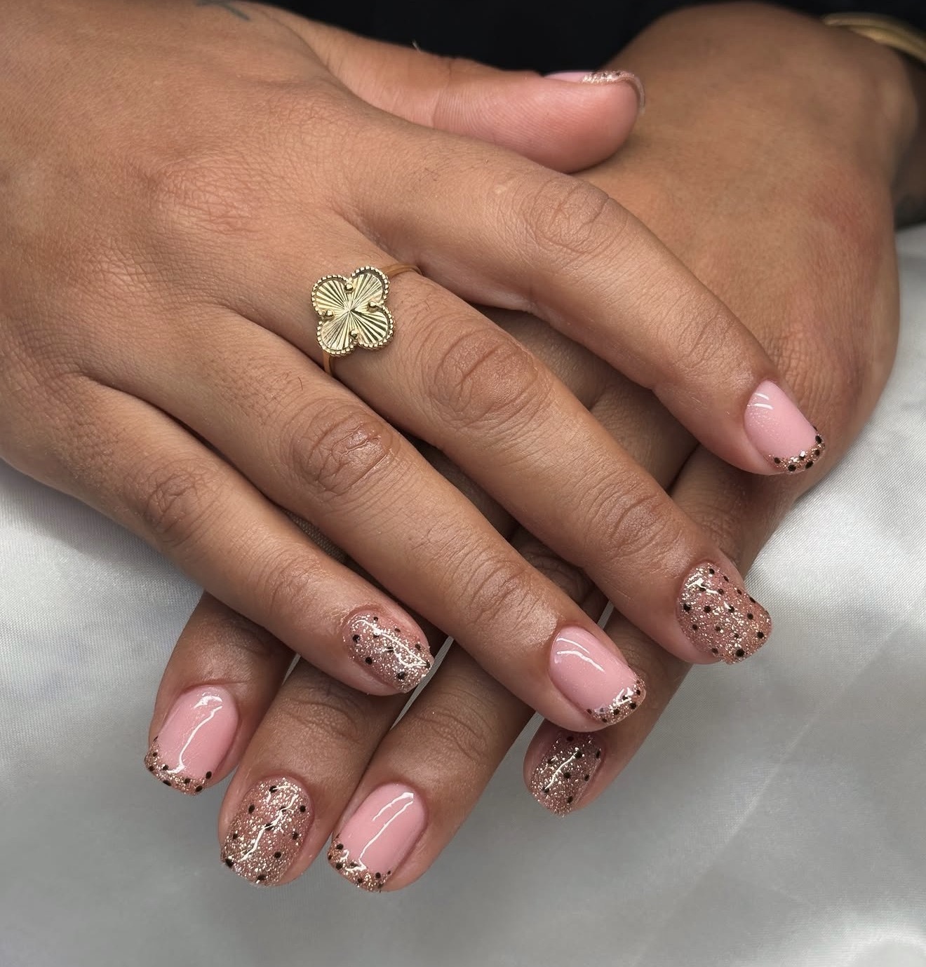 Nude BIAB-nagels met glitter en zwarte stipjes, een gouden klavertjesring